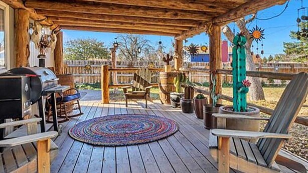 A covered outdoor patio with a wooden deck, a grill, and a seating area with chairs and a table.