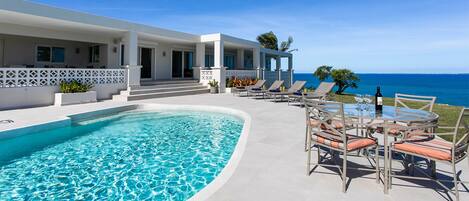 A modern resort with a swimming pool, outdoor seating, and a view of the ocean.