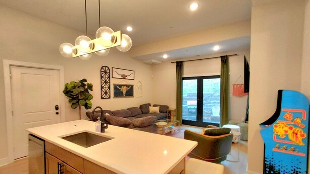 Una cocina moderna con una isla central, un comedor con sofá y sillas, y una sala de estar con sofá y televisor.