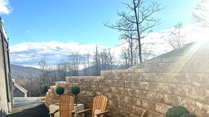 Un patio con sillas Adirondack de madera, un brasero y una jardinera con un árbol pequeño.