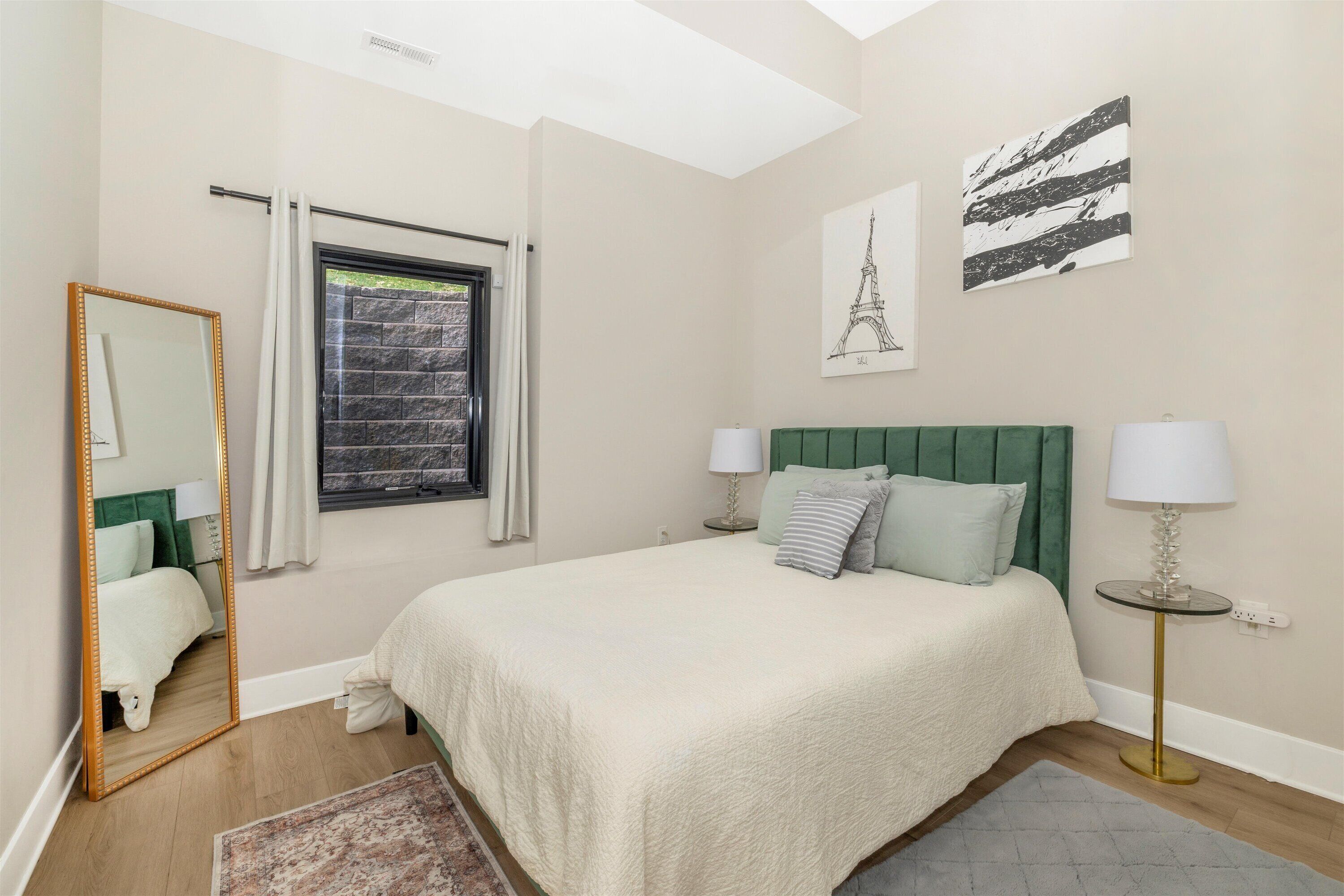 A bedroom with a large bed, two bedside tables with lamps, a mirror, and artwork on the walls.