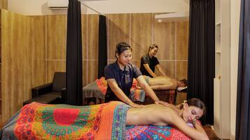 A massage therapy room with wooden panel walls, a massage table, and two practitioners attending to a client.