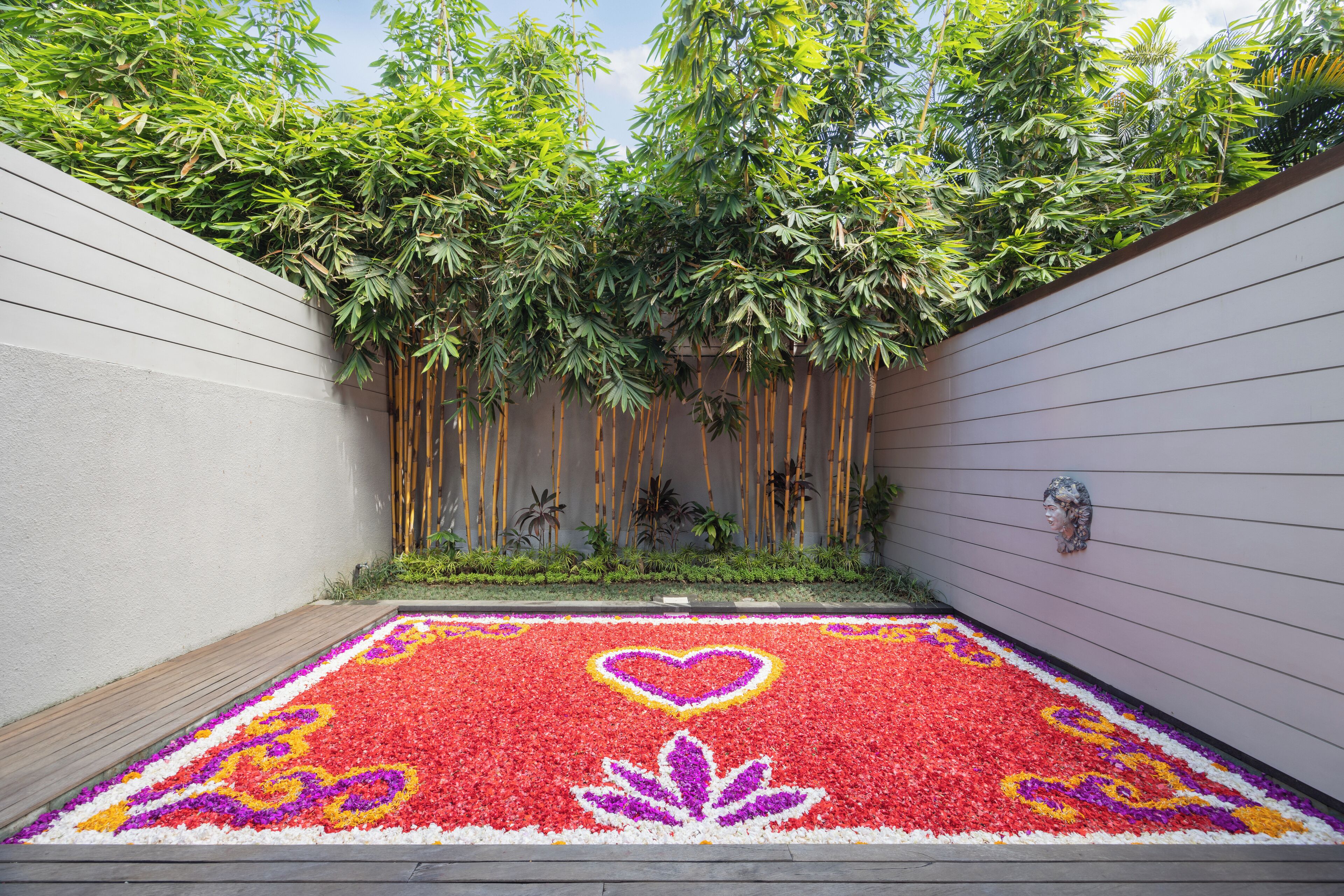 A courtyard with a patterned flower carpet, bamboo plants, and a decorative wall.