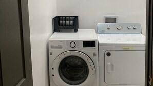 A laundry room with a front-loading washer and dryer, a black laundry basket, and a thermostat on the dryer.