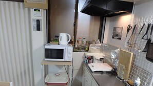 Une cuisine compacte équipée d’un micro-ondes, d’un grille-pain et d’une machine à café placés sur une étagère, d’un évier et de divers ustensiles de cuisine accrochés au mur.