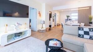 A modern living room with a flat-screen TV, a white entertainment unit, a sofa, and a dining area with a table and chairs. - 2-Bedroom Apartment with Terrace and Side Sea View (Cannes)