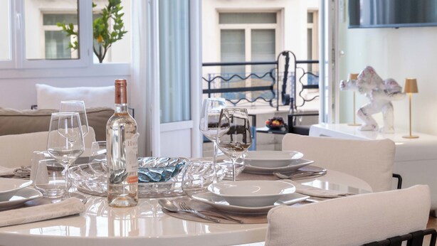 A dining table set with plates, glasses, and a bottle, with a view of a balcony and building in the background. - 2-Bedroom Apartment with Terrace and Side Sea View (Cannes)