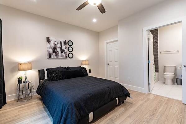 A bedroom with a bed, bedside lamps, a ceiling fan, a door, and a bathroom visible through an open door.