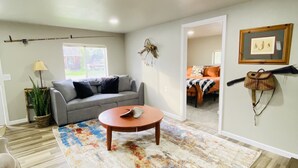 A living room with a grey sofa, a round coffee table, a colorful rug, a plant, and a wall-mounted picture frame. - Hooked On The River (Stites)