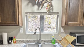A kitchen with wooden cabinets, a double sink, a window, and a microwave. - Hooked On The River (Stites)