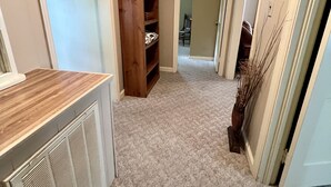 A narrow hallway with a wooden shelving unit, a radiator, and a clock on the wall.