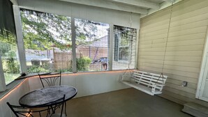 A covered patio with a table and chairs, a bench, and a view of a residential area through large windows.