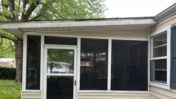 A single-story house with a covered porch, a screened door, and a window with blinds.