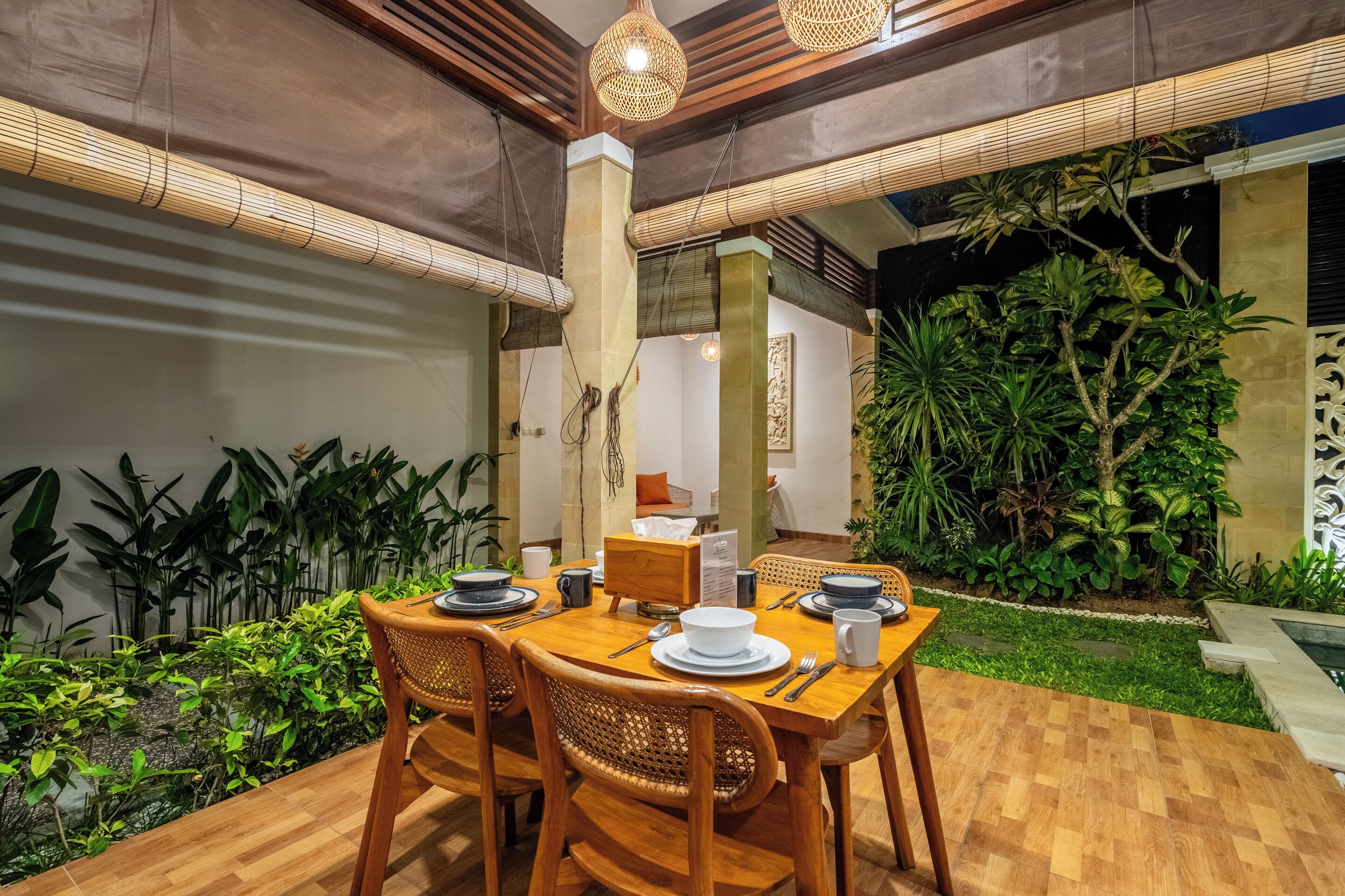 Un comedor con una mesa de madera dispuesta para cuatro personas, rodeada de sillas de mimbre.