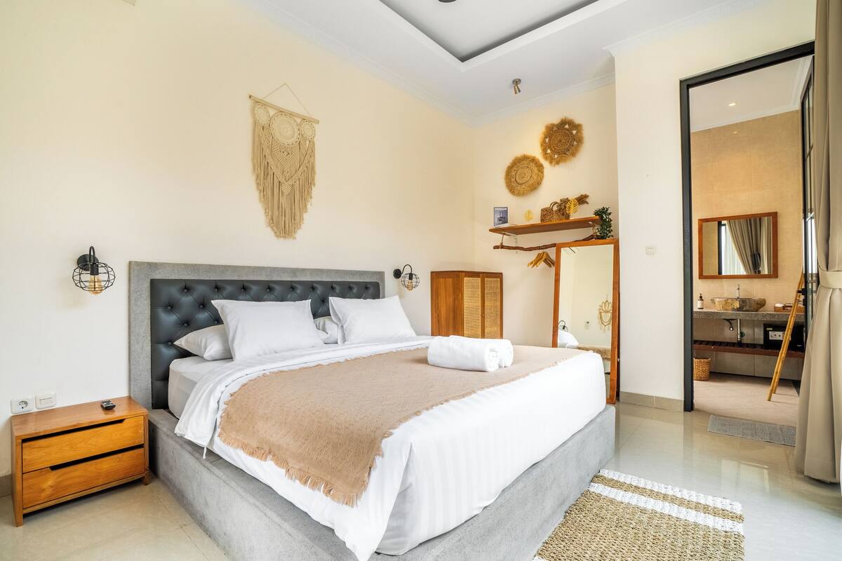 A modern bedroom with a large bed, bedside tables, a wardrobe, and a view into the bathroom.