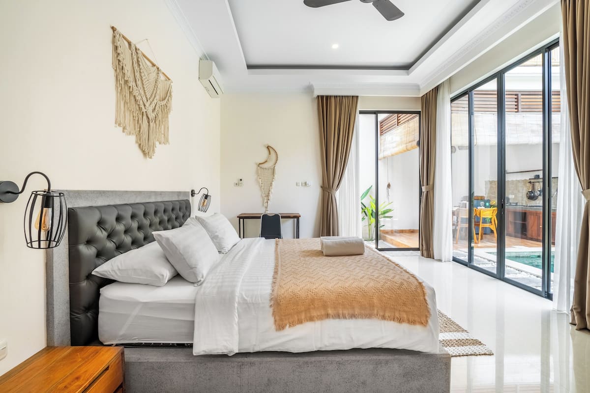 A modern bedroom with a large bed, a ceiling fan, and a view of a pool through large windows.