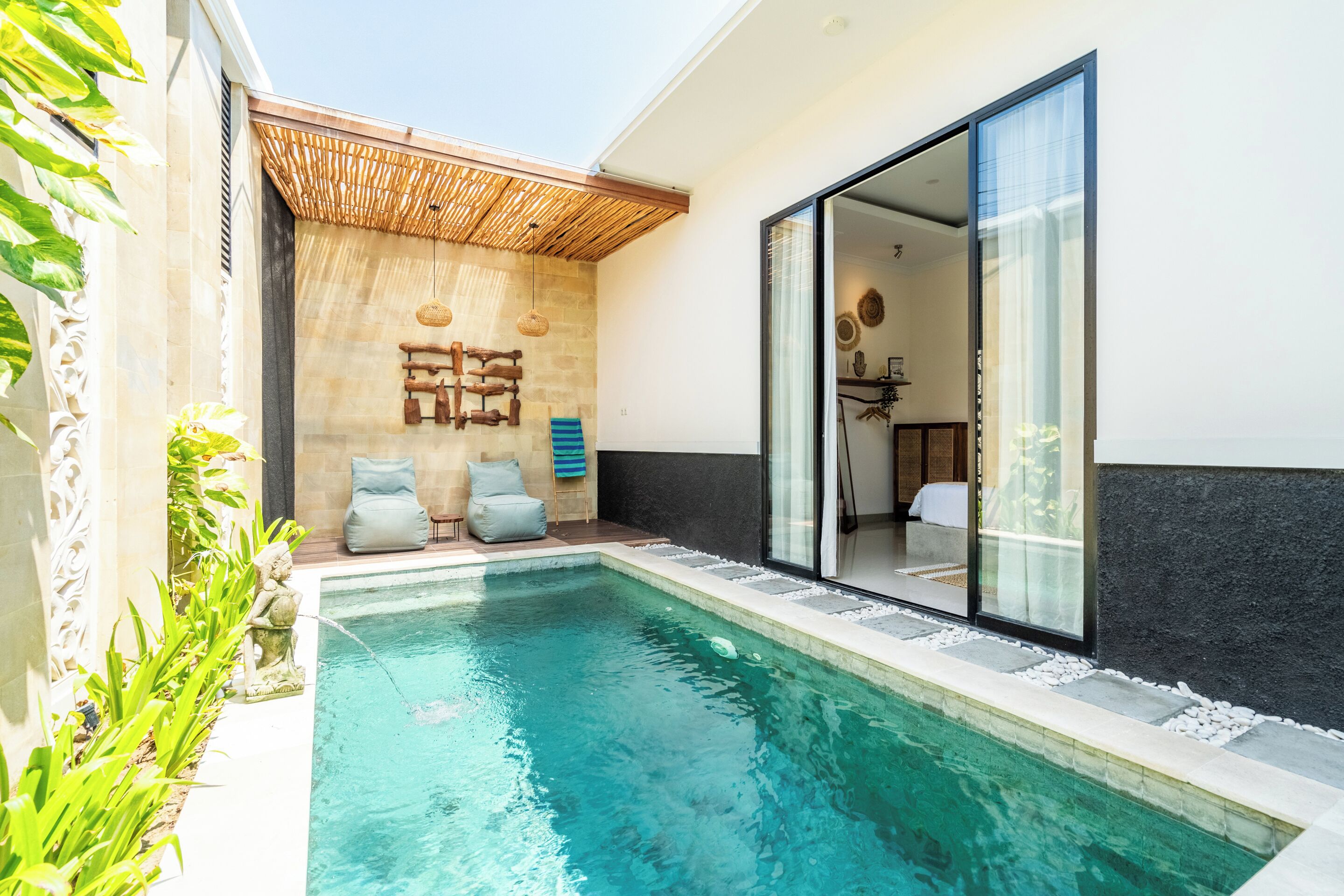 A modern outdoor pool area with a stone wall, wooden seating, and a glass door leading to a room.