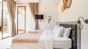 A modern bedroom with a large bed, a television, a wall-mounted light fixture, and a decorative wall piece. - Villa Kamaratih (Legian)