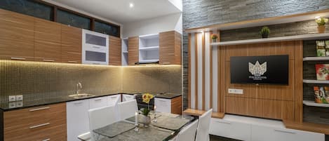 Una cucina moderna con mobili in legno, schienale piastrellato e zona pranzo con tavolo e sedie in vetro.