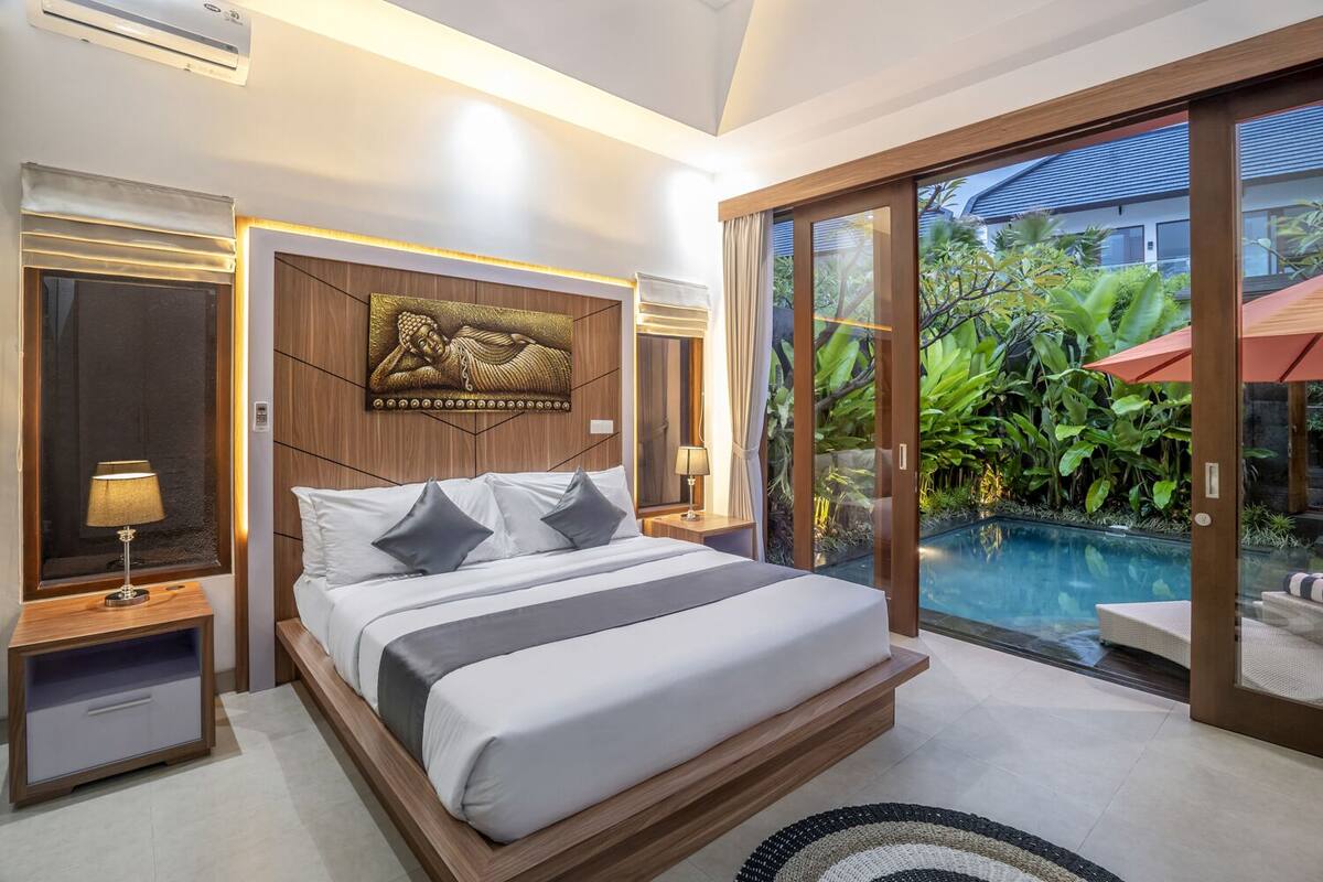 A modern bedroom with a large bed, a wooden headboard, and a view of a swimming pool.