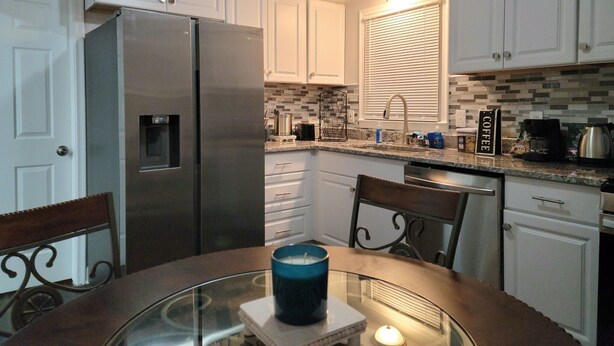 Una cocina compacta con armarios blancos, un refrigerador de acero inoxidable, salpicadero de azulejos y una cafetera sobre la encimera.