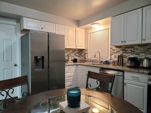 A compact kitchen with white cabinets, a stainless steel refrigerator, a tiled backsplash, and a coffee maker on the countertop.