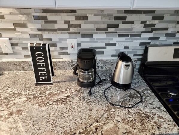 A kitchen counter with a coffee maker, a kettle, and a sign that reads "COFFEE".