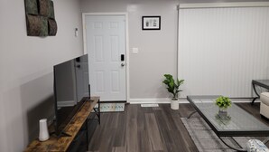 Una sala moderna con un banco de madera, una mesa de centro de vidrio, un sofá y un televisor sobre un mueble.