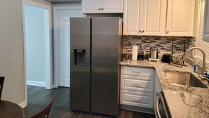Cocina compacta con armarios blancos, refrigerador de acero inoxidable, pileta integrada y salpicadero de azulejos.