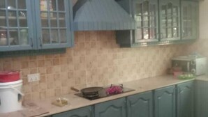 A kitchen with teal cabinets, a tiled backsplash, and a central range hood. - Impeccable 4-Bed Villa in Mirpur azad khasmir (Mirpur azad khasmir)