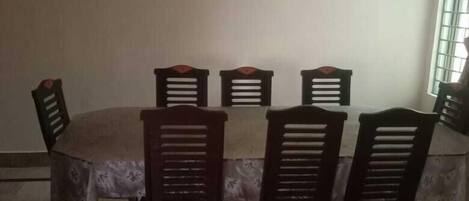 A dining area with a table and six chairs, a window with bars, and a plain wall.