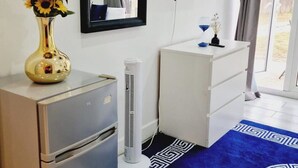 A room with a white dresser, a small white cabinet, a blue patterned rug, and a vase with sunflowers on the dresser.