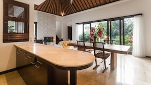 A modern kitchen with a large island, wooden ceiling, and large windows with a view of greenery. - Villa Jade (Ungasan)