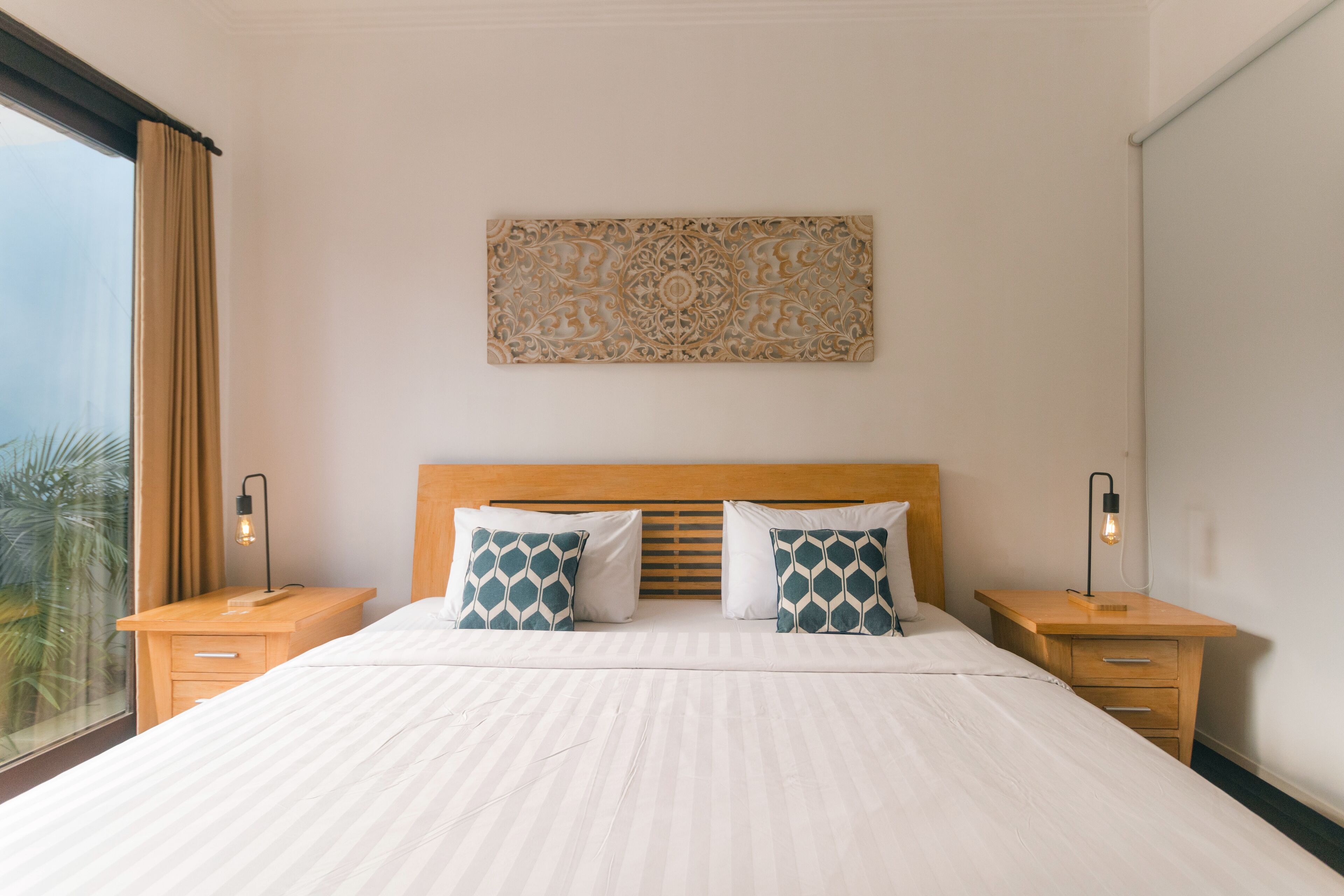 A hotel room with a large bed, two bedside tables, a headboard, and a decorative wall piece.