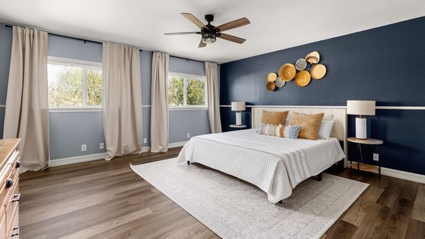 Une chambre à coucher comprenant un lit, un ventilateur de plafond, une table de chevet avec une lampe et un mur décoré d’assiettes.