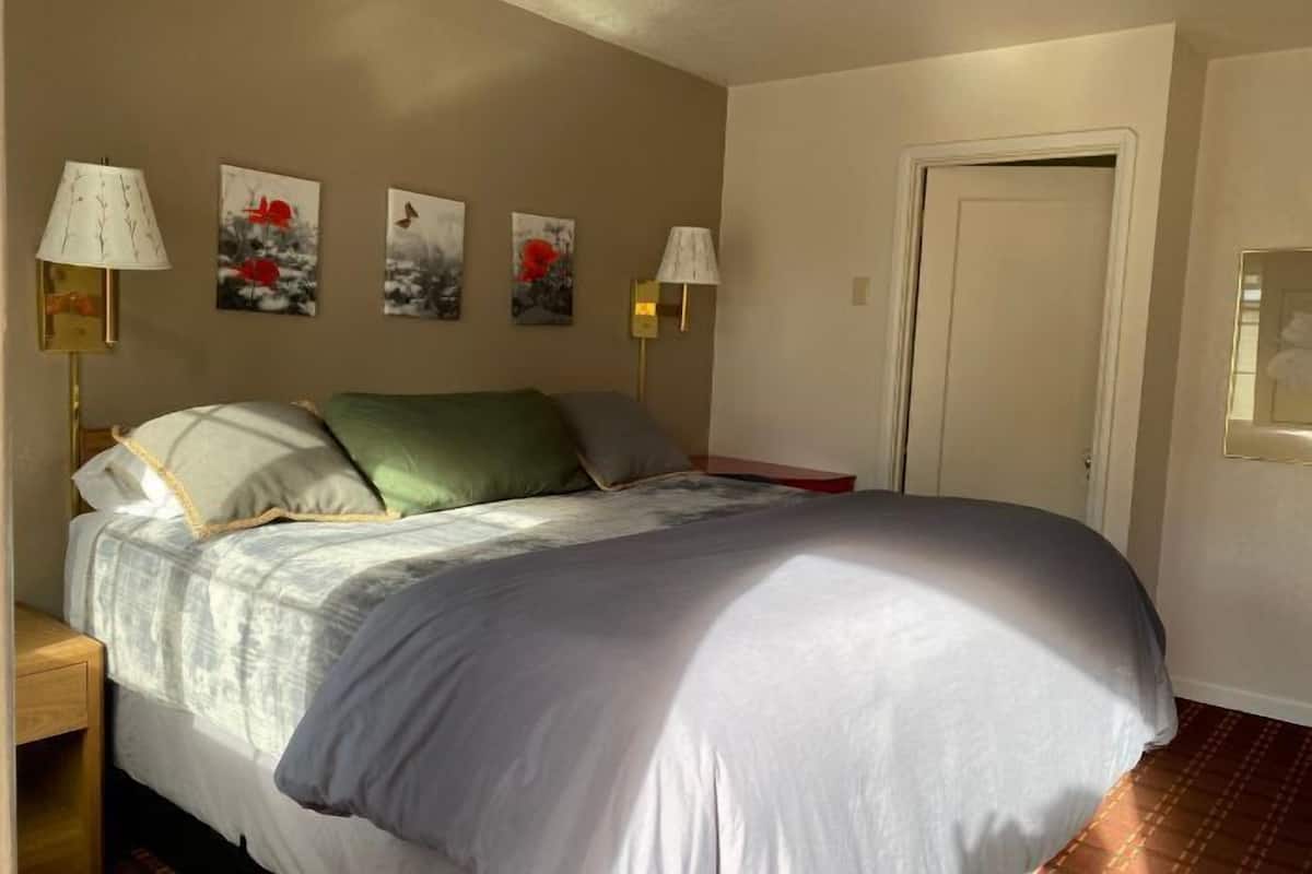 A bedroom with a large bed, two bedside lamps, and four wall-mounted paintings.