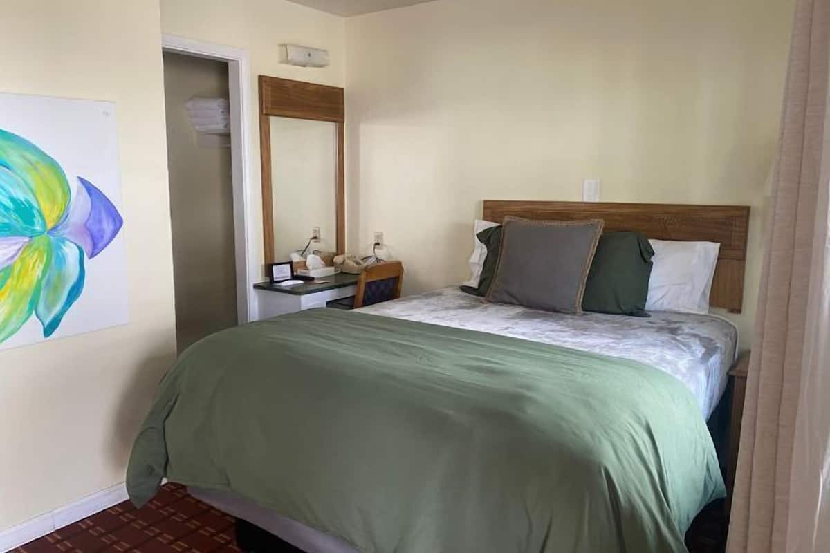 A hotel room with a bed, a bedside table, a mirror, and a wall painting.
