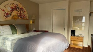 A bedroom with a large bed, a bedside table with a lamp, a wooden dresser, and a decorative fan on the wall. - Monte Bianco Inn (Mount Shasta)
