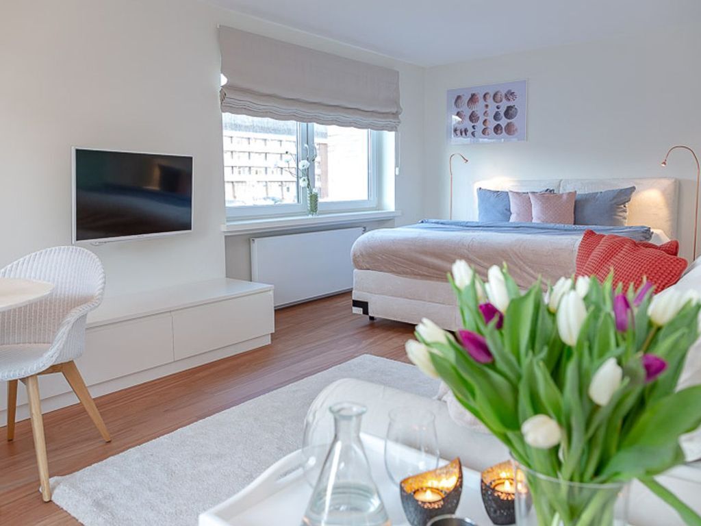Een moderne slaapkamer met een bed, nachtkastje en een aan de muur bevestigde televisie.