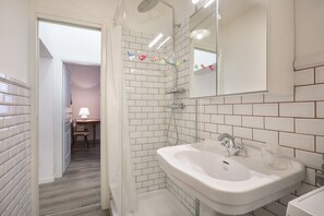 A bathroom with white tiled walls, a white sink, and a shower.