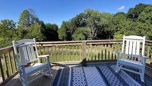 Une terrasse en bois avec deux fauteuils Adirondack blancs et un tapis à motifs.