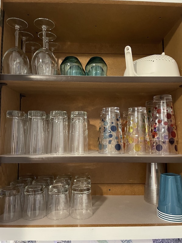 Una estantería con diferentes tipos de cristalería, como copas de vino, vasos y frascos decorativos.