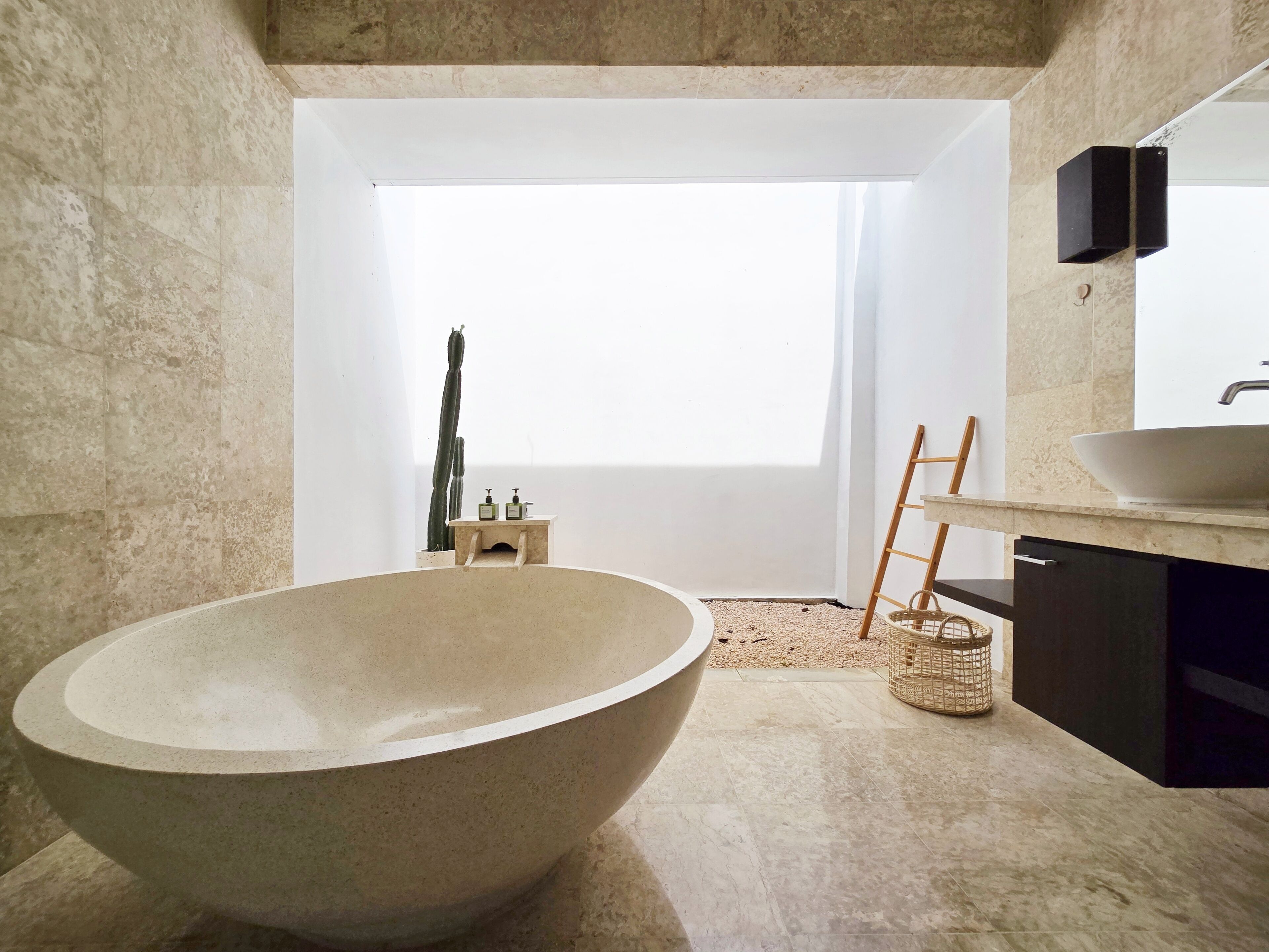 Un baño moderno con una bañera independiente grande, un lavabo minimalista y un ventanal que aporta luz natural.