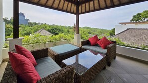 A covered outdoor seating area with wicker furniture and cushions, overlooking a lush landscape and distant buildings. - Villa Venta (Ungasan)
