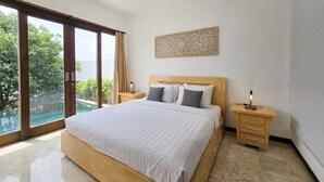 A bedroom with a large bed, a nightstand, a wall-mounted lamp, and a view of a swimming pool. - Villa Venta (Ungasan)