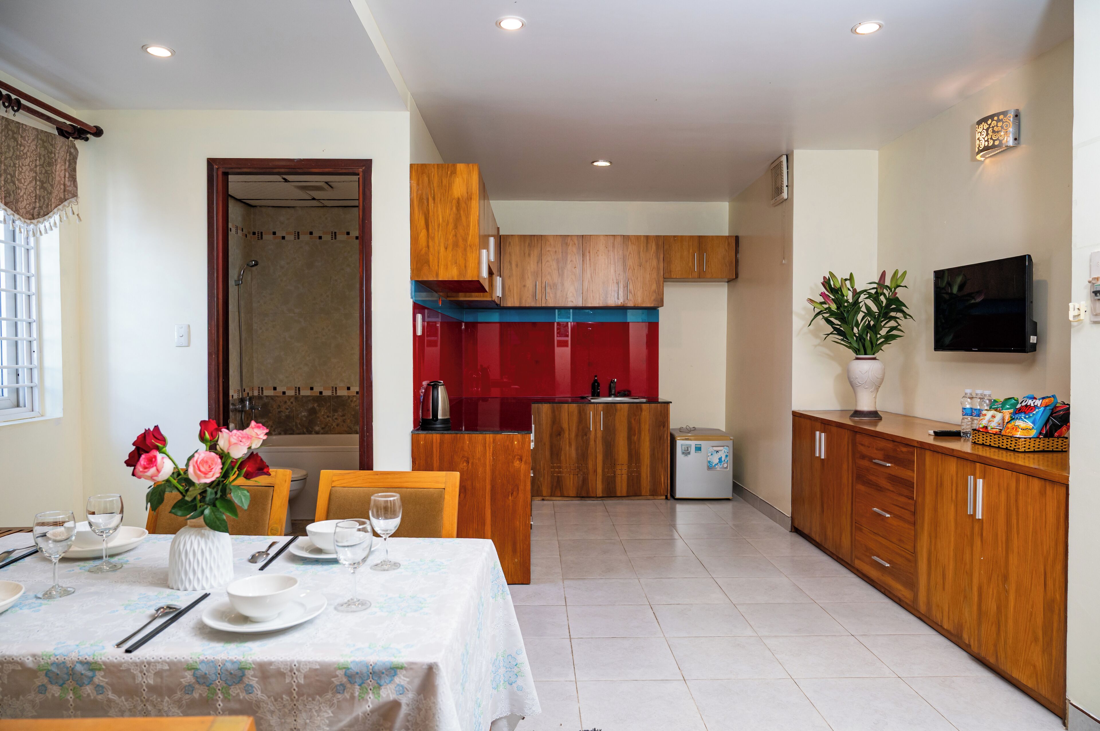 A modern kitchen with wooden cabinets, a red backsplash, and a dining area with a table set for two.