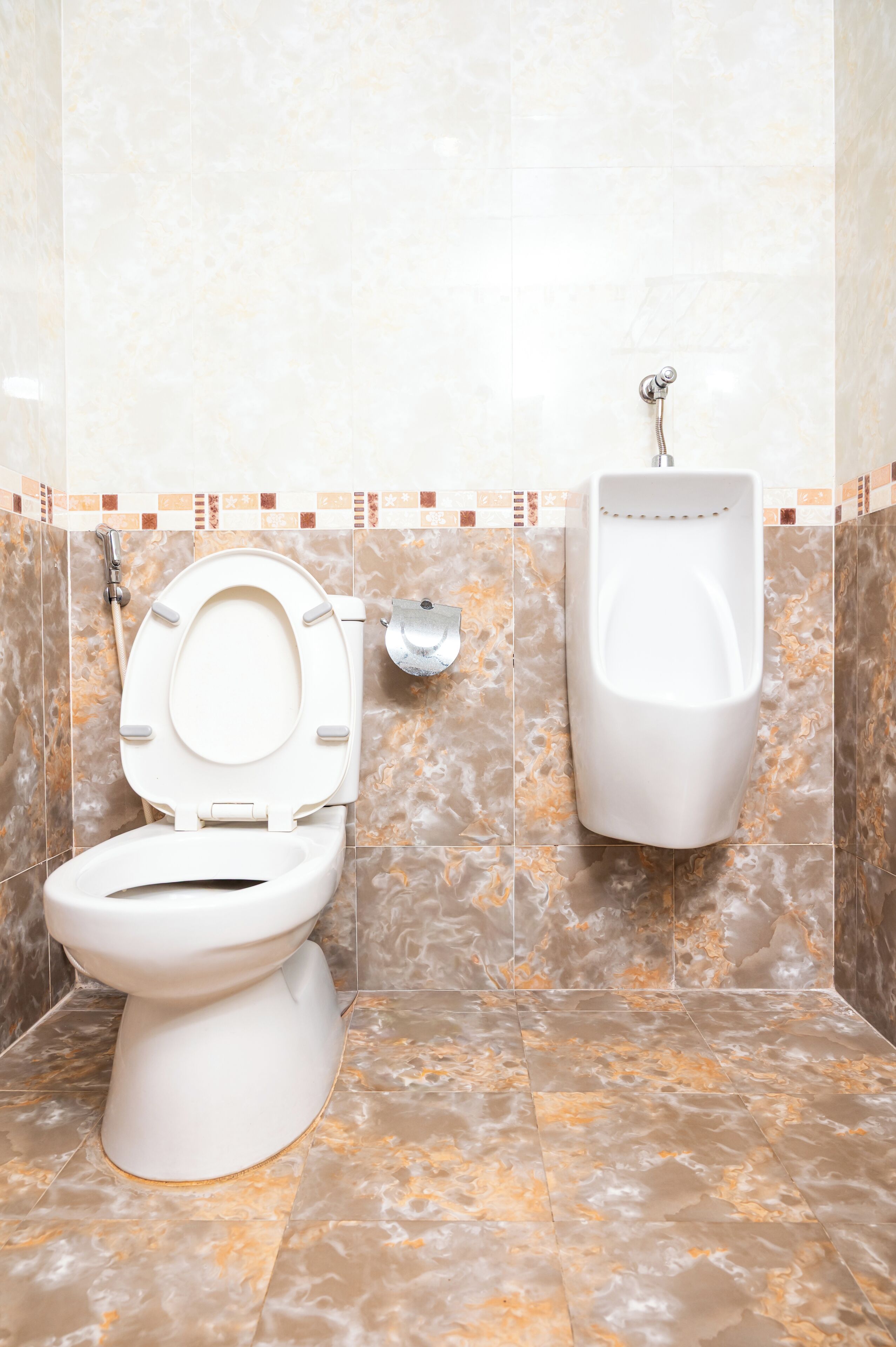 A bathroom with a toilet, urinal, and marble tiles.
