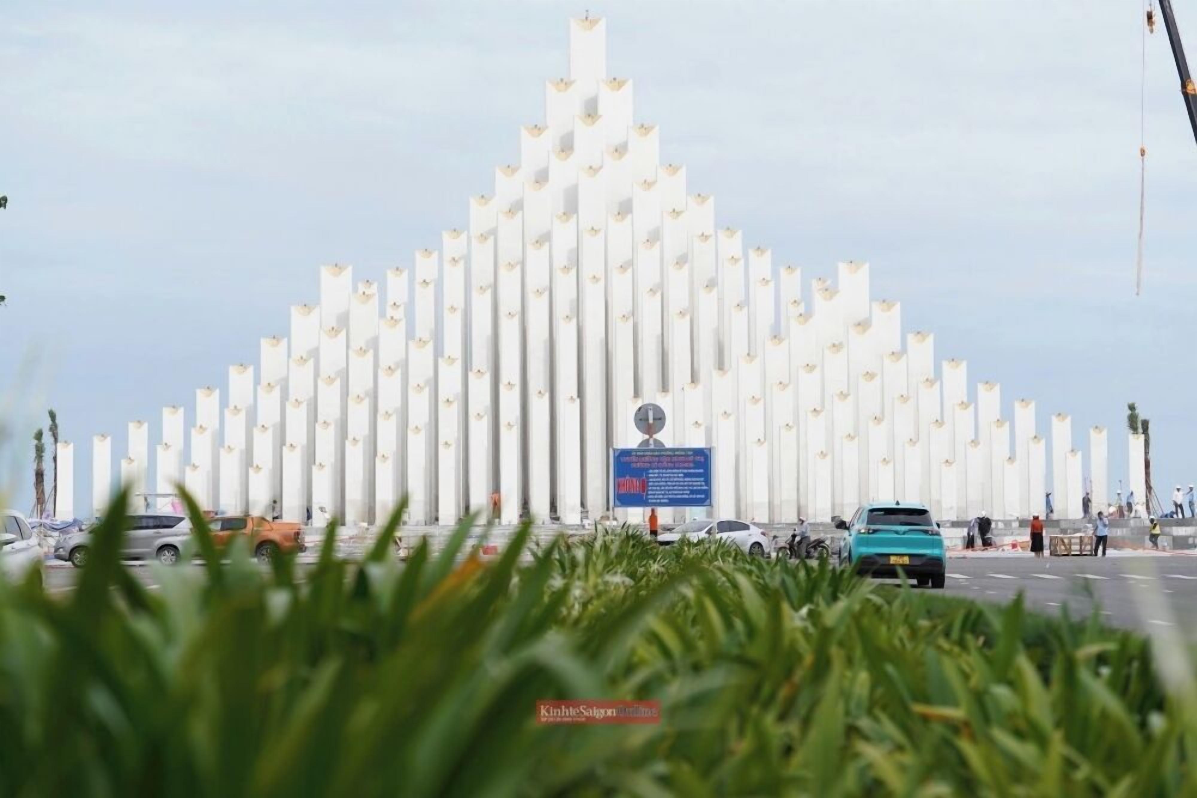 A large, symmetrical structure with vertical elements, possibly a monument or memorial, with a sign in the center.