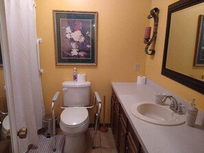 Bathroom features a toilet, sink, and shower, with a framed floral painting on the wall.