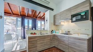 Eine moderne Küche mit Holzausbau, einer eingebauten Mikrowelle und einem großen Fenster mit Blick auf eine Terrasse.
